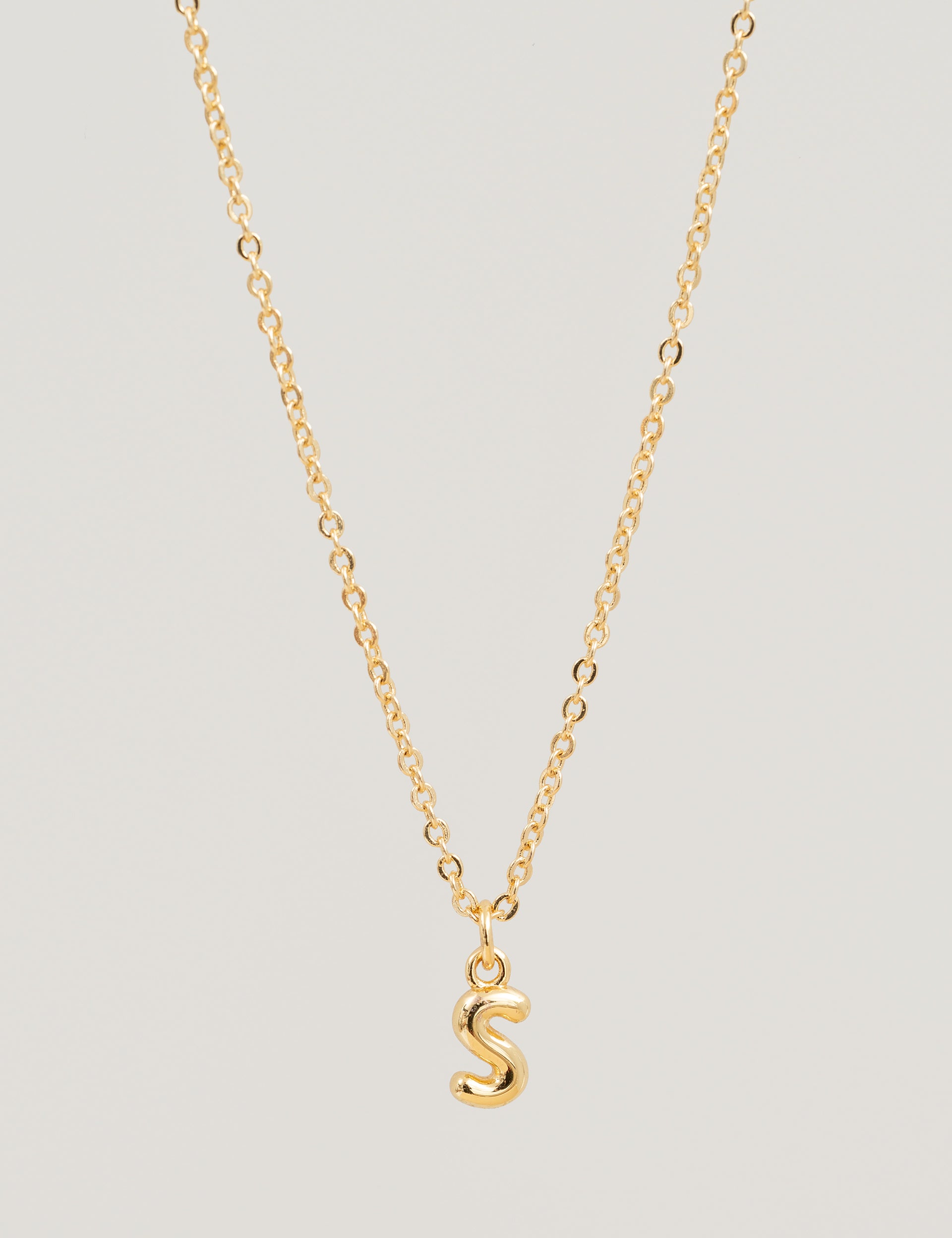 Gold necklace with a 'S' pendant on a light gray background