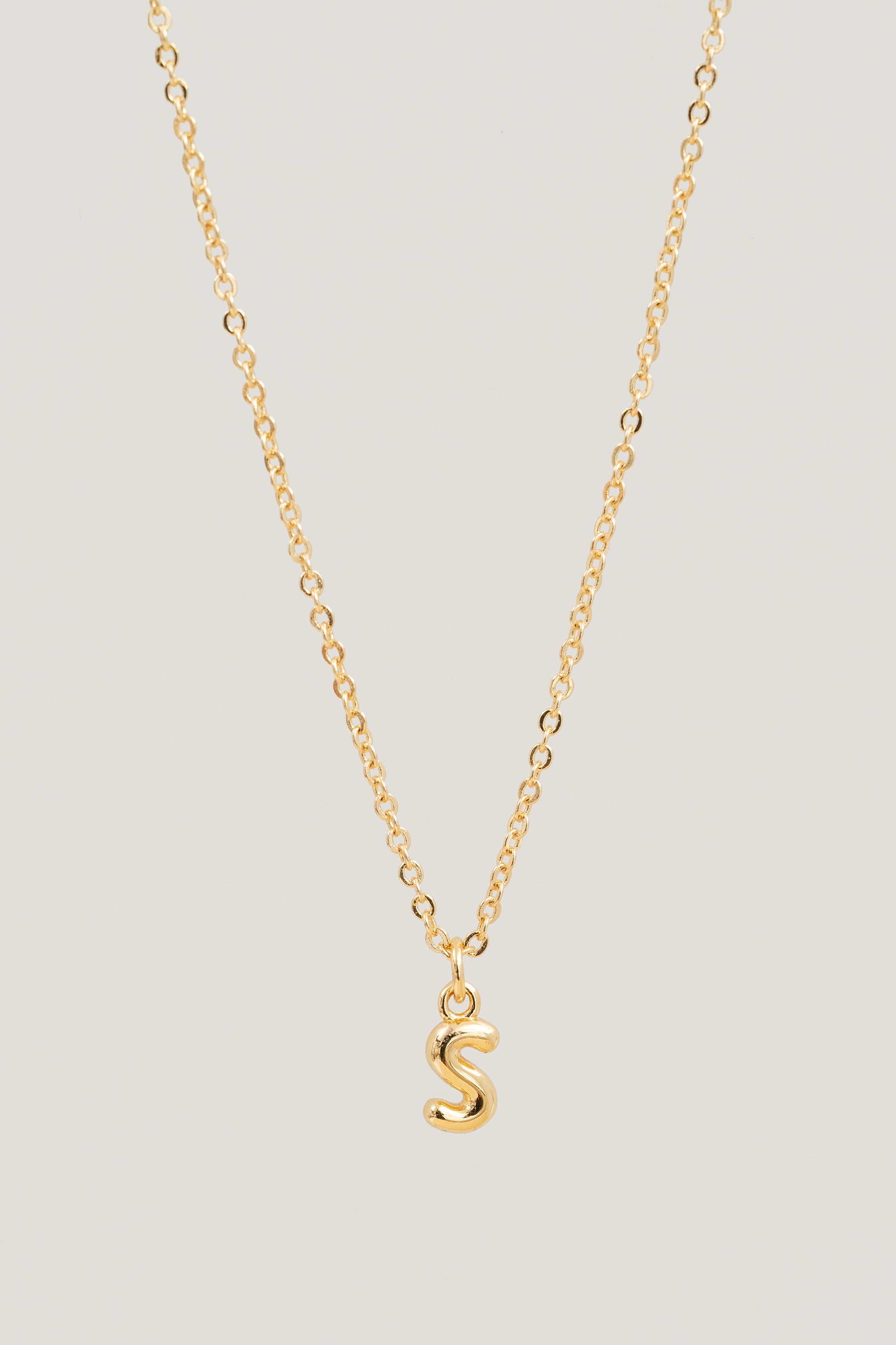 Gold necklace with a 'S' pendant on a light gray background