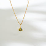 Gold necklace with a green gemstone pendant on a white background