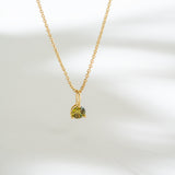 Gold necklace with a green gemstone pendant on a white background