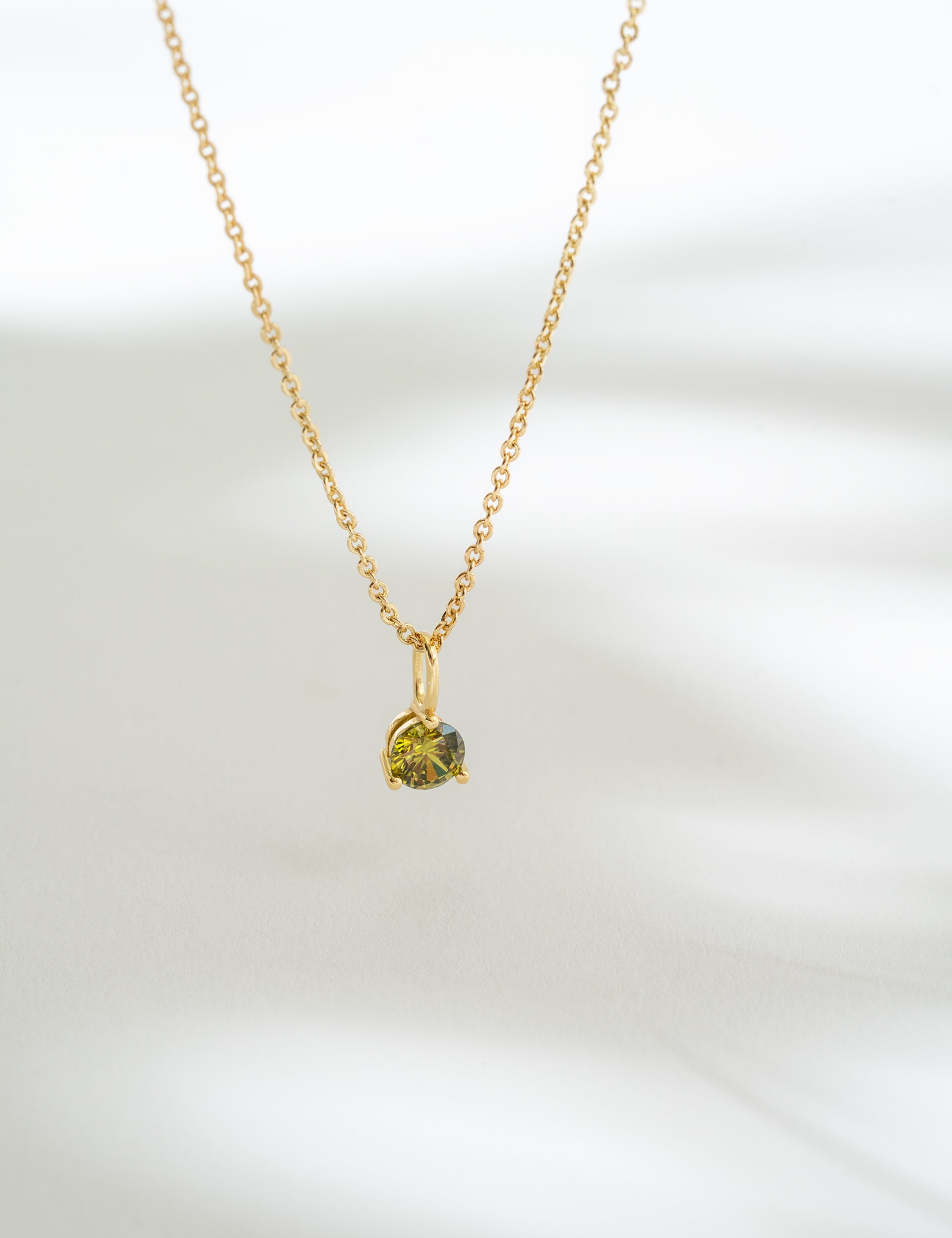 Gold necklace with a green gemstone pendant on a white background