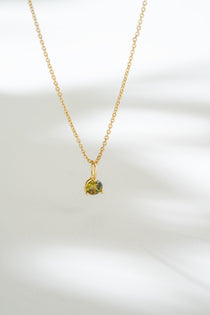 Gold necklace with a green gemstone pendant on a white background