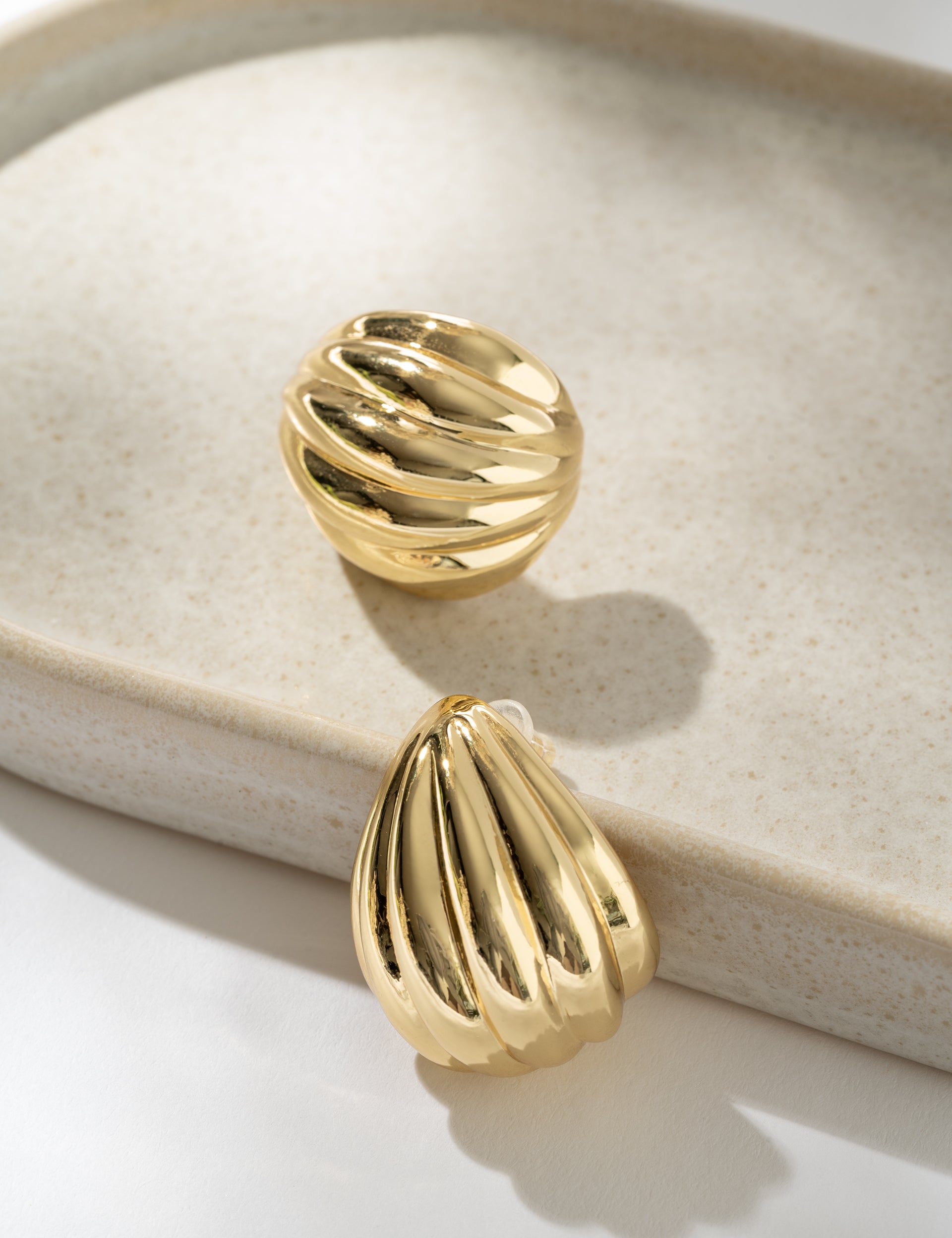 Gold earrings on a beige jewelry dish