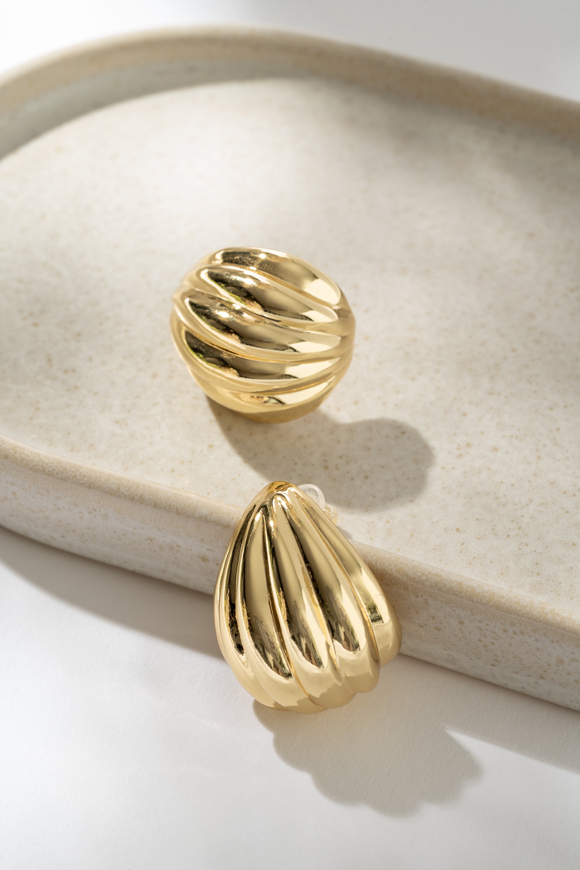 Gold earrings on a beige jewelry dish