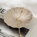 Gold bracelet on a shell-shaped dish with a magazine in the background