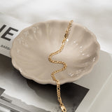 Gold bracelet on a shell-shaped dish with a magazine in the background