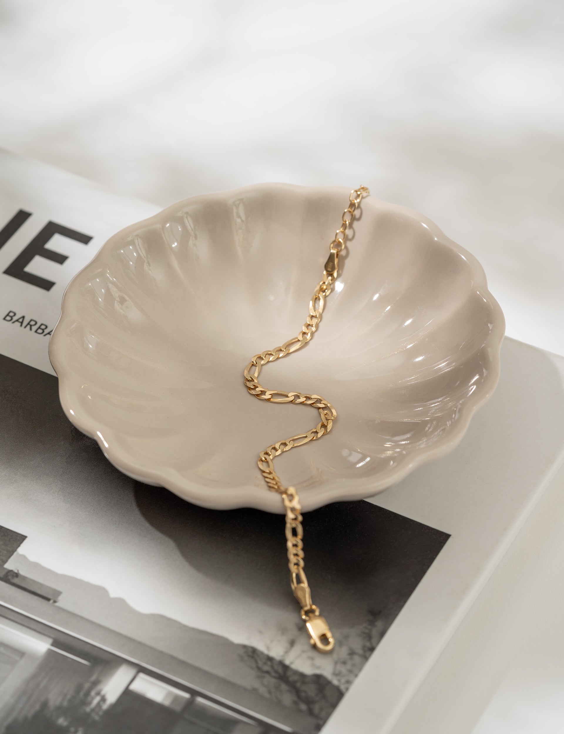 Gold bracelet on a shell-shaped dish with a magazine in the background