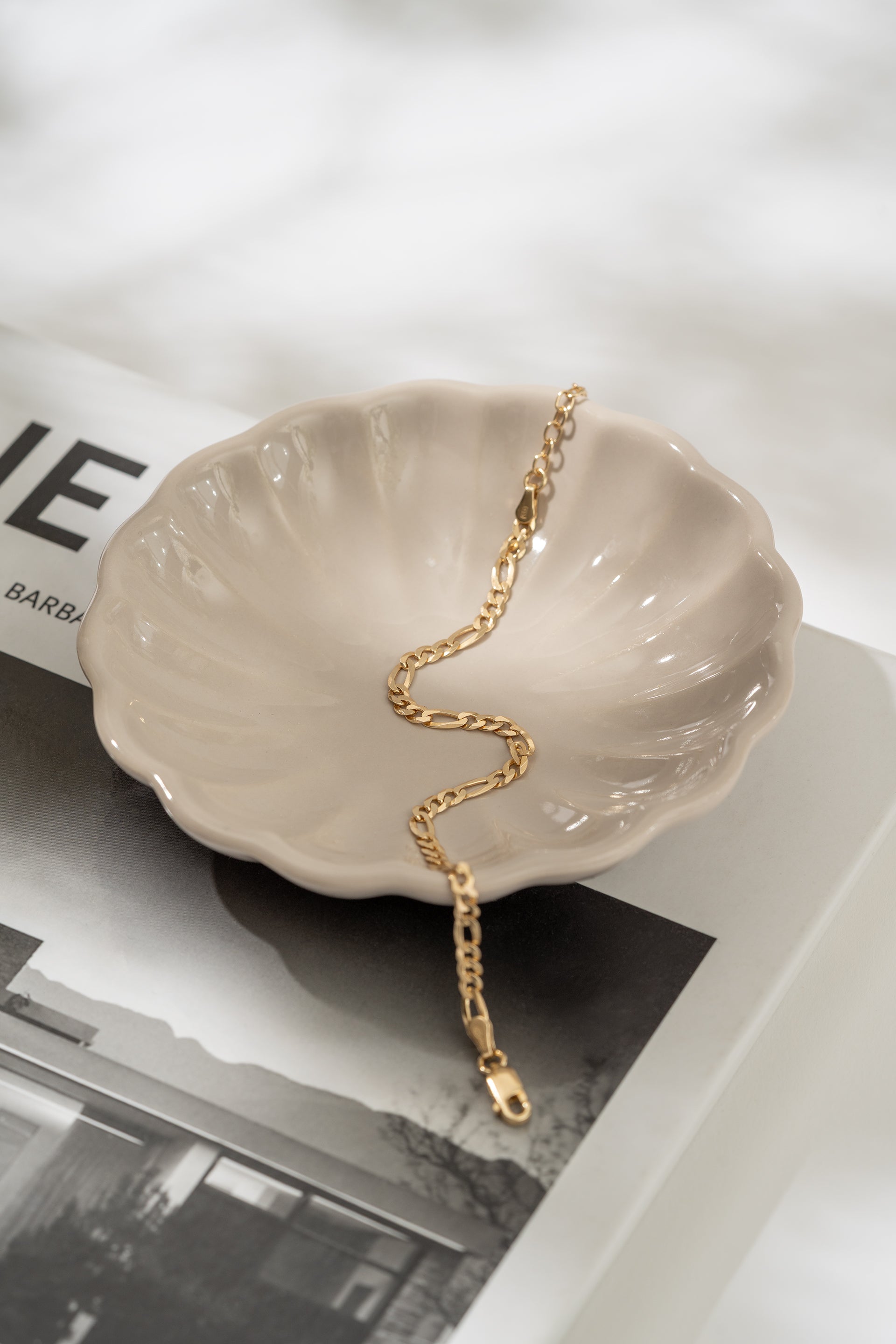Gold bracelet on a shell-shaped dish with a magazine in the background