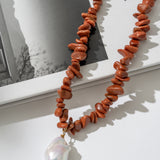 Necklace with red beads and a pearl pendant on a white surface