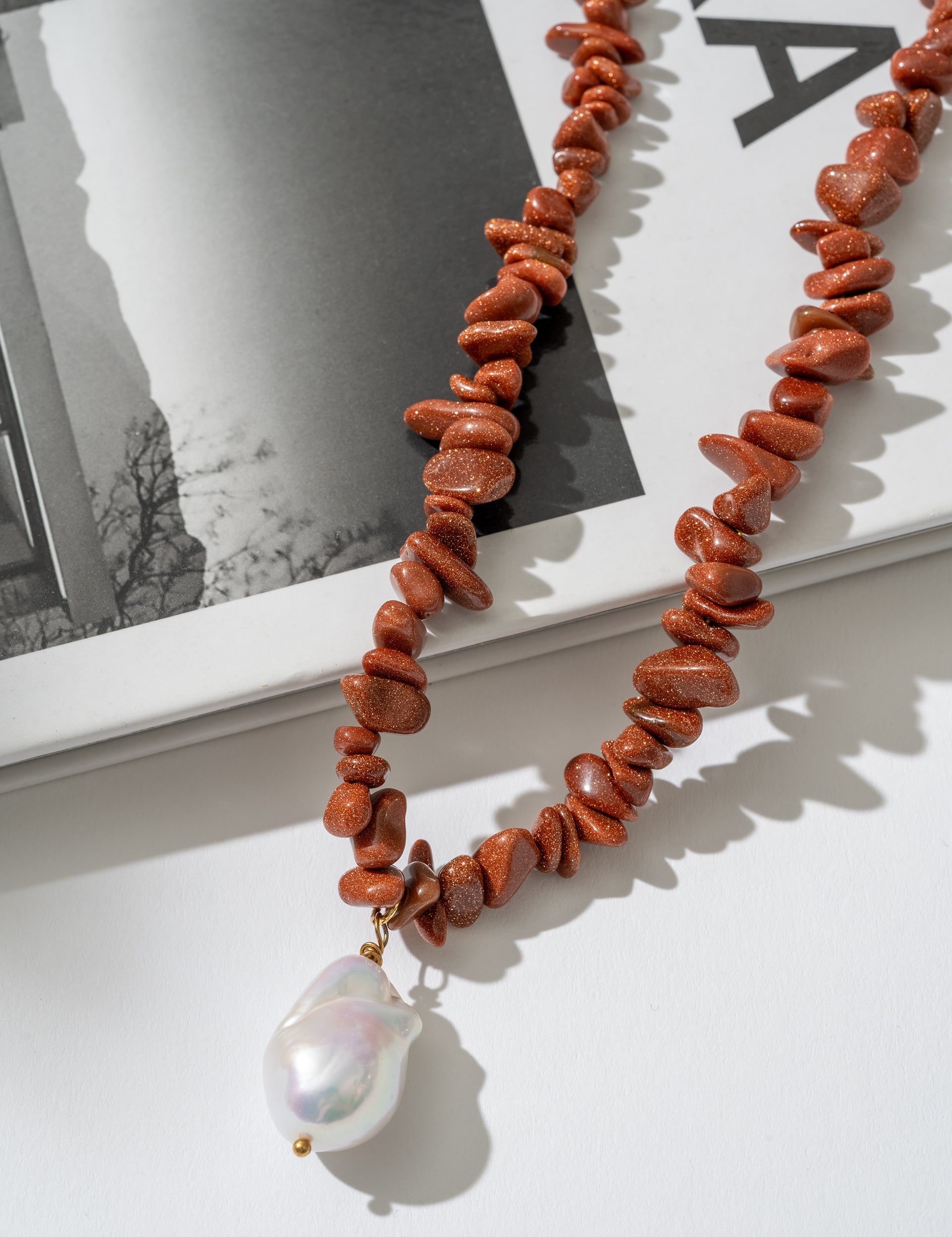 Necklace with red beads and a pearl pendant on a white surface