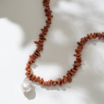 Necklace with red beads and a white pearl on a light background