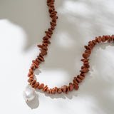 Necklace with red beads and a white pearl on a light background