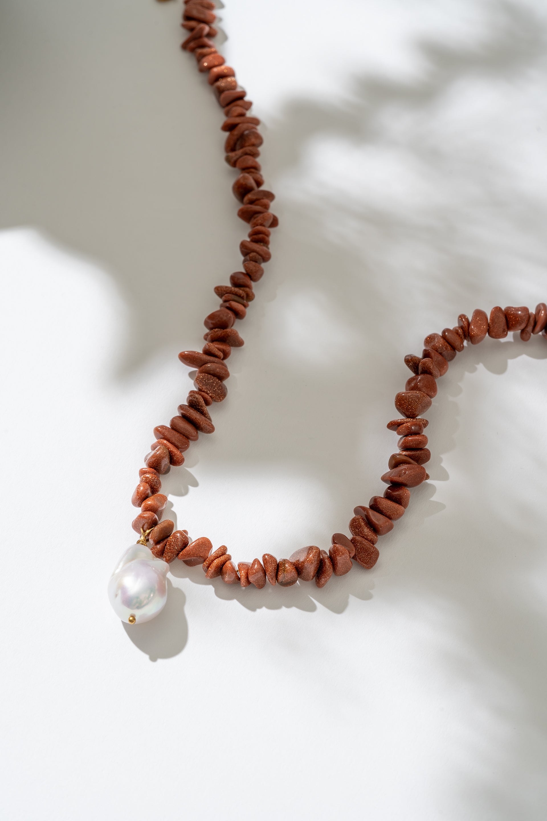 Necklace with red beads and a white pearl on a light background