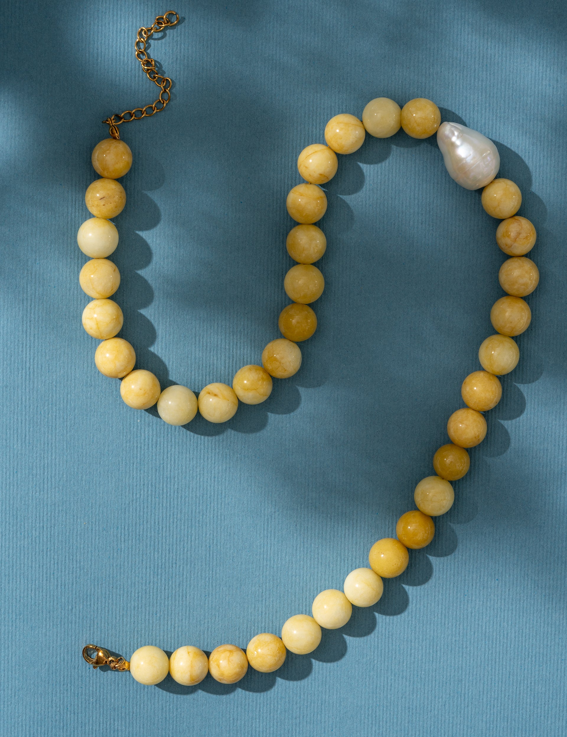 Beaded yellow necklace with a pearl on a blue background