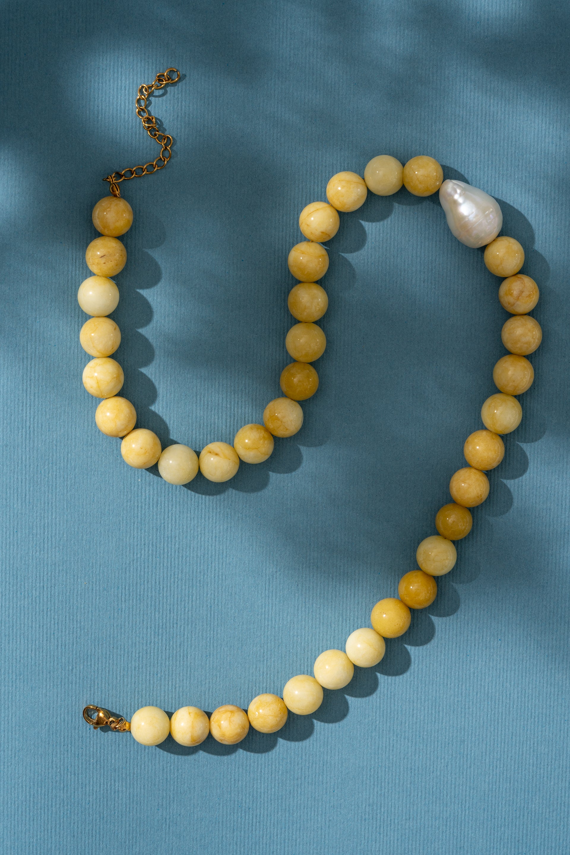 Beaded yellow necklace with a pearl on a blue background