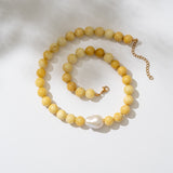 Yellow beaded necklace with a pearl pendant on a white background