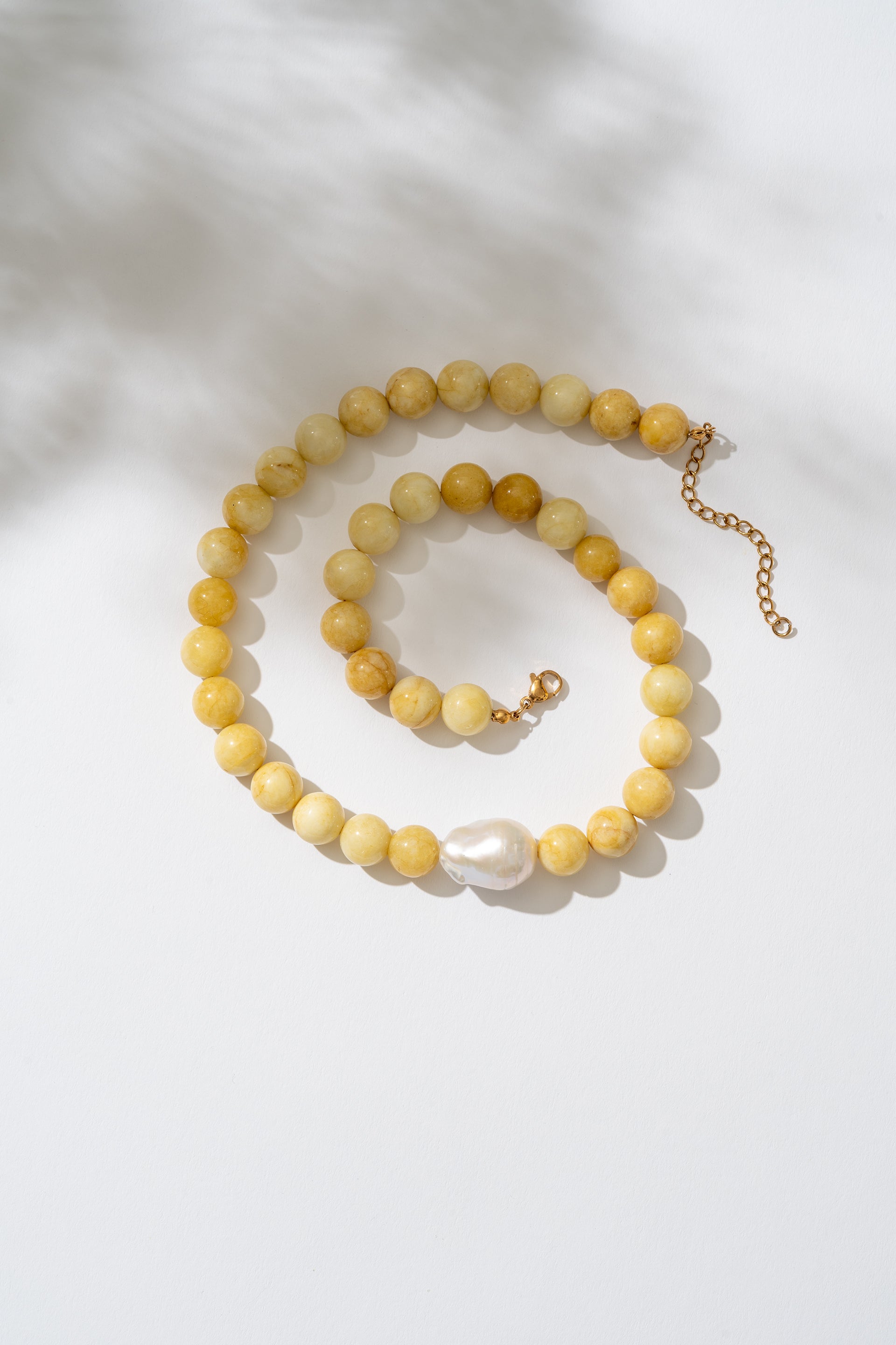 Yellow beaded necklace with a pearl pendant on a white background