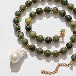 Green beaded necklace with a gold chain and white pendant on a light background