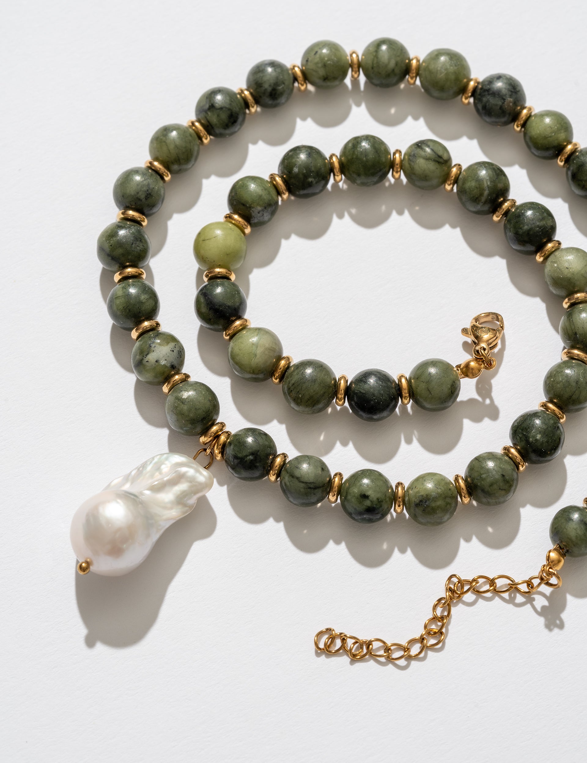 Green beaded necklace with a gold chain and white pendant on a light background