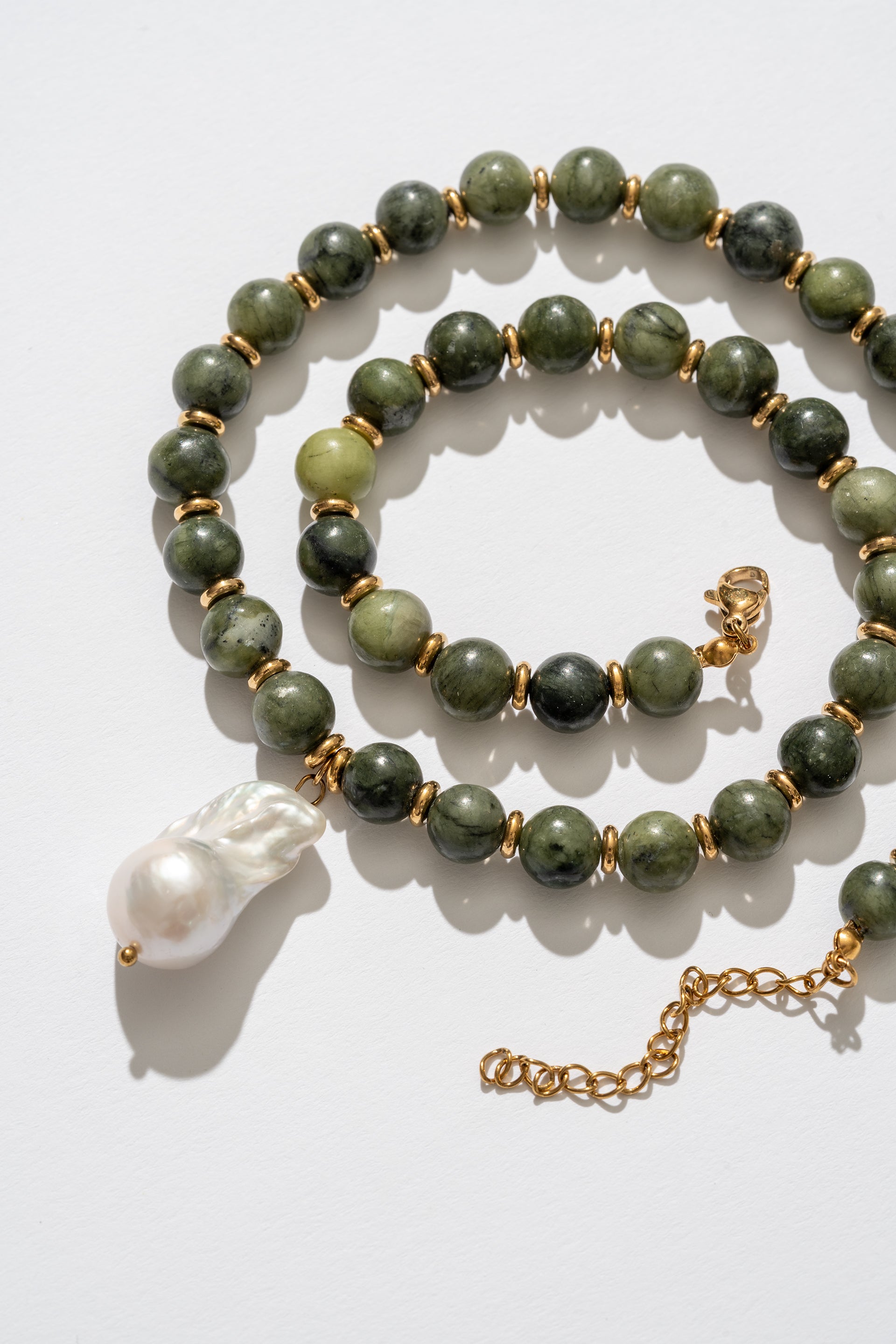 Green beaded necklace with a gold chain and white pendant on a light background