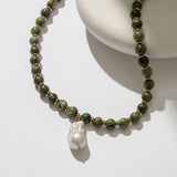 Necklace with green beads and a pearl pendant on a white surface