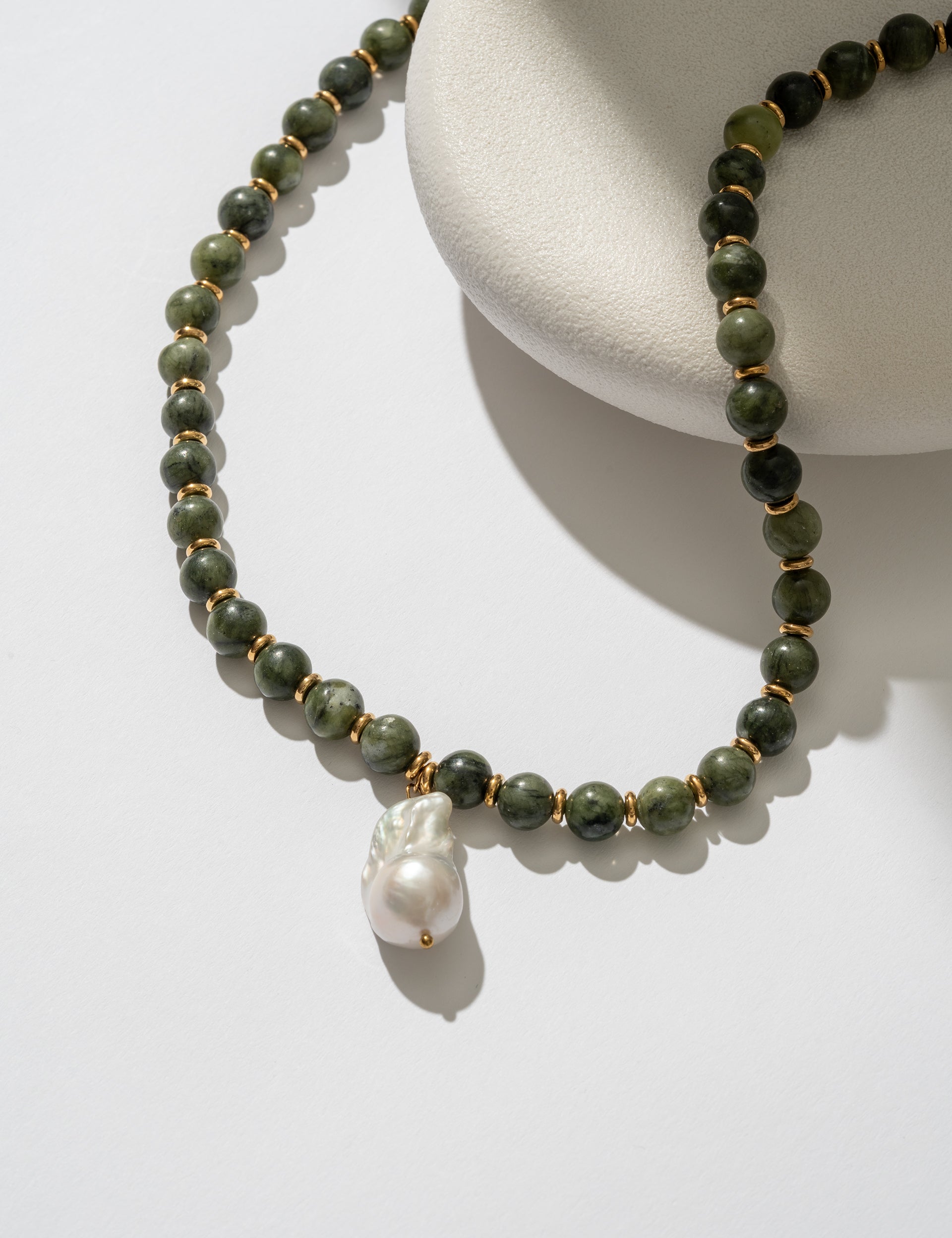 Necklace with green beads and a pearl pendant on a white surface