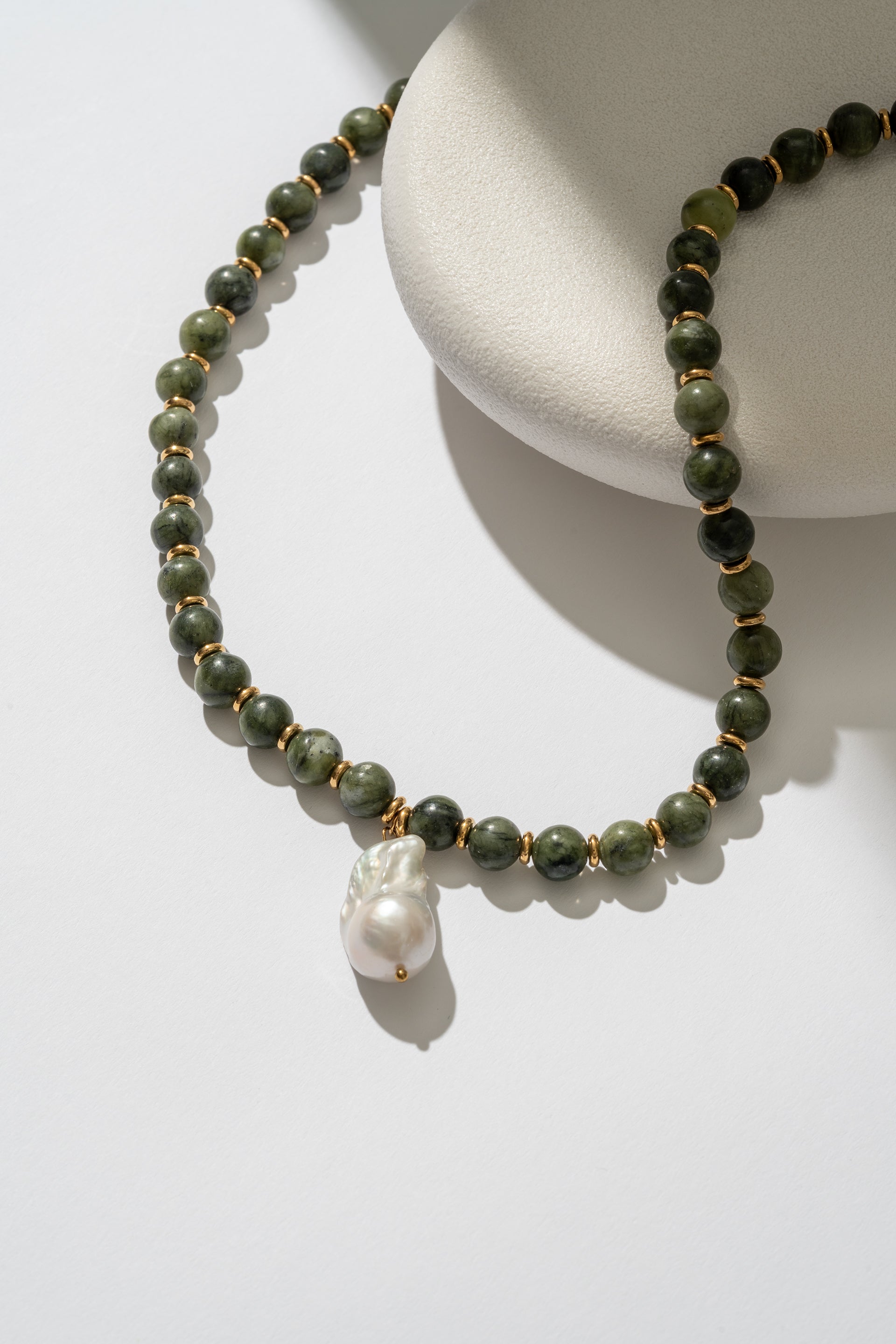 Necklace with green beads and a pearl pendant on a white surface