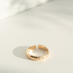 Gold flower patterned ring on a light gray surface with soft shadows