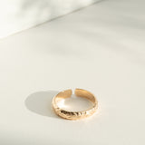 Gold flower patterned ring on a light gray surface with soft shadows
