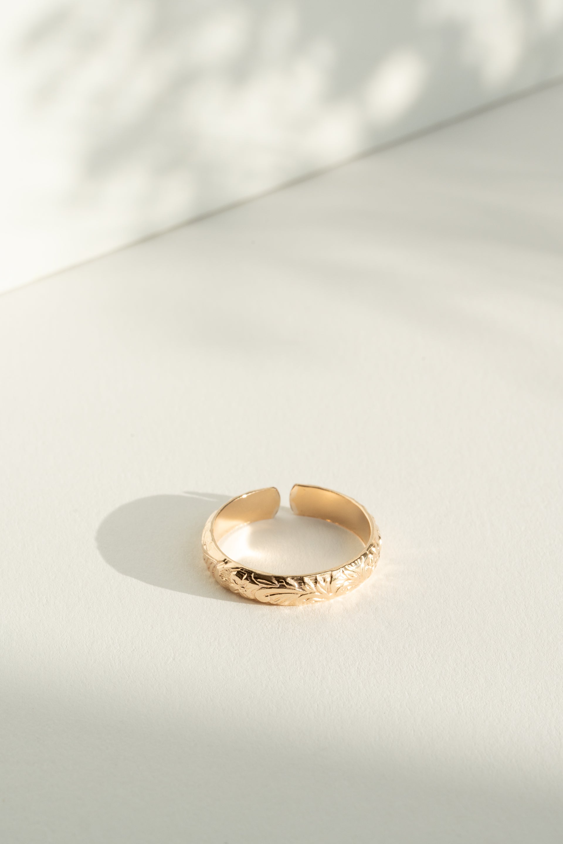 Gold flower patterned ring on a light gray surface with soft shadows