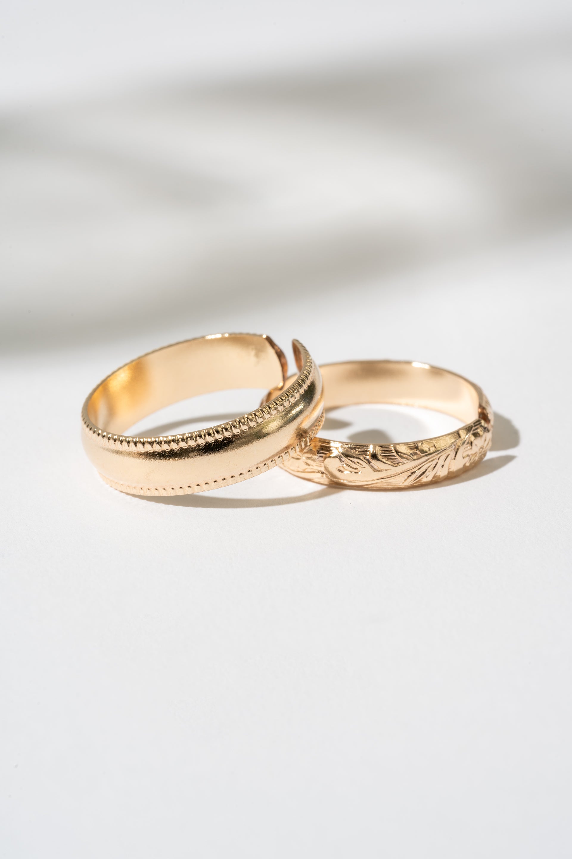 Two gold rings with intricate designs on a light background