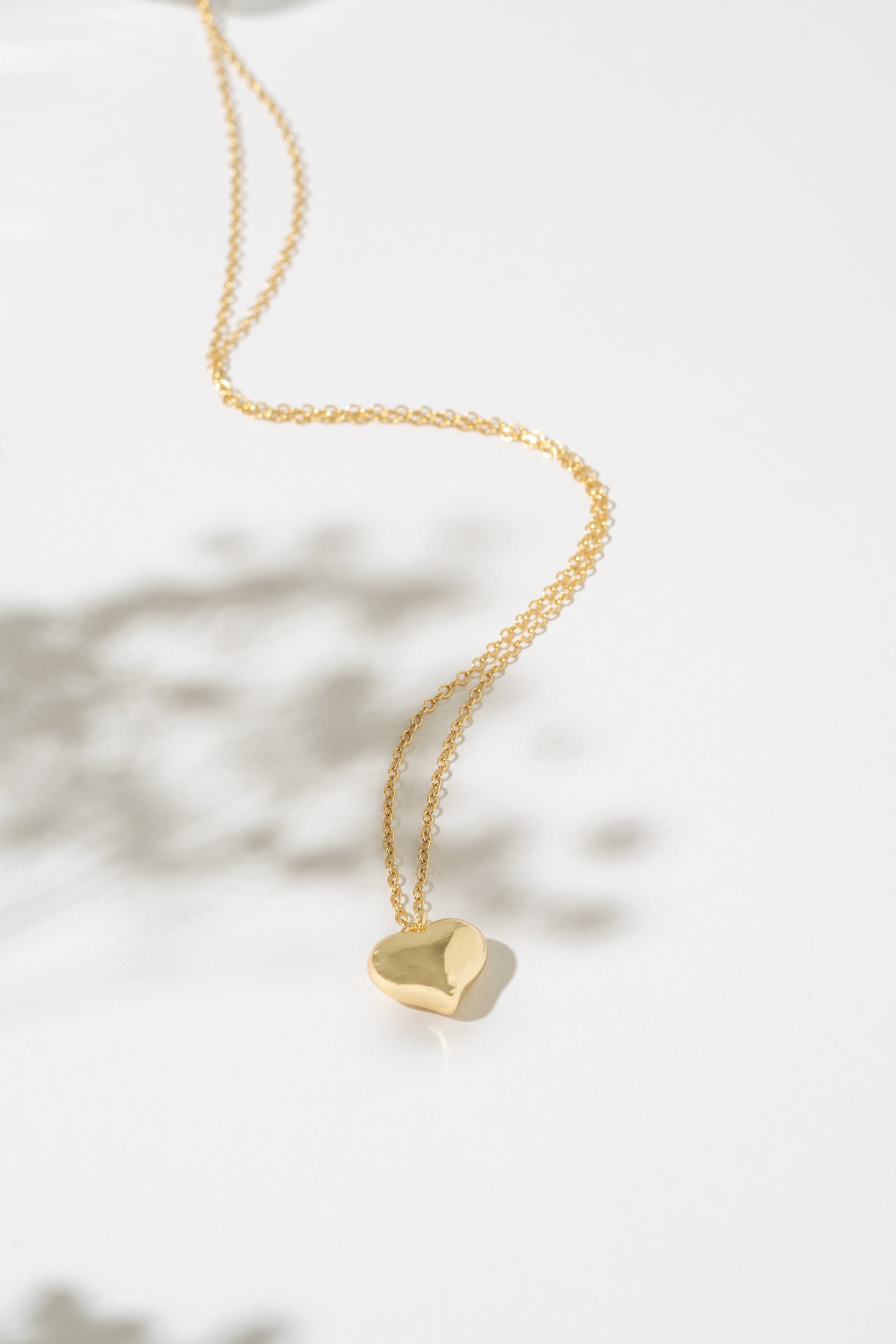 Gold necklace with a heart-shaped pendant on a white background