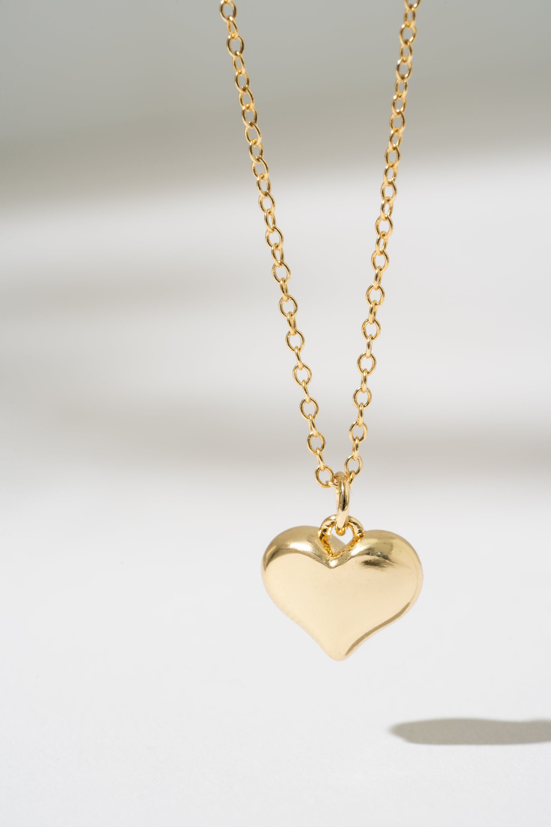 Gold heart-shaped pendant necklace on a light gray background