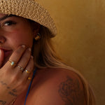 Woman wearing a straw hat and gold jewelry against a beige background
