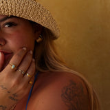 Woman wearing a straw hat and gold jewelry against a beige background