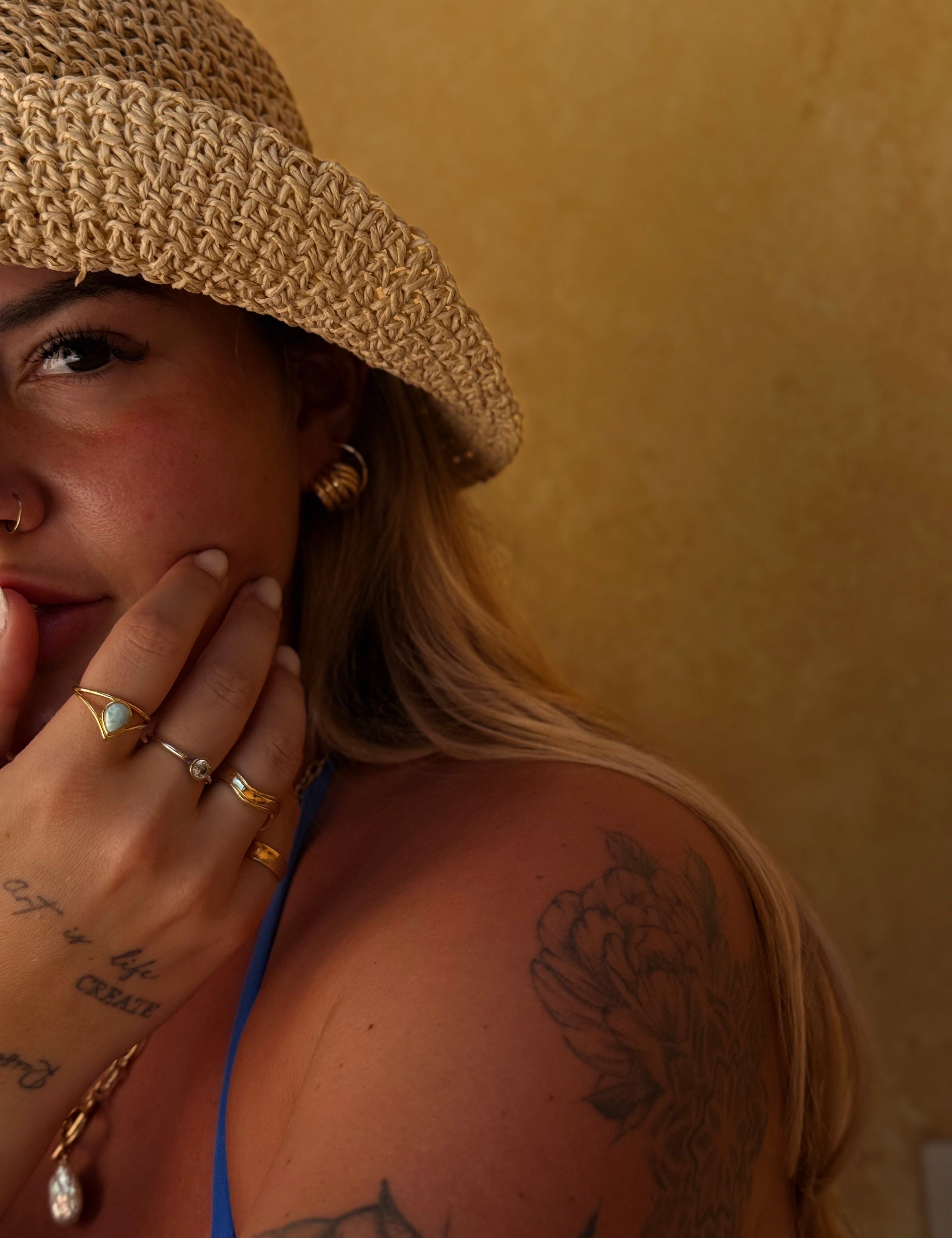 Woman wearing a straw hat and gold jewelry against a beige background