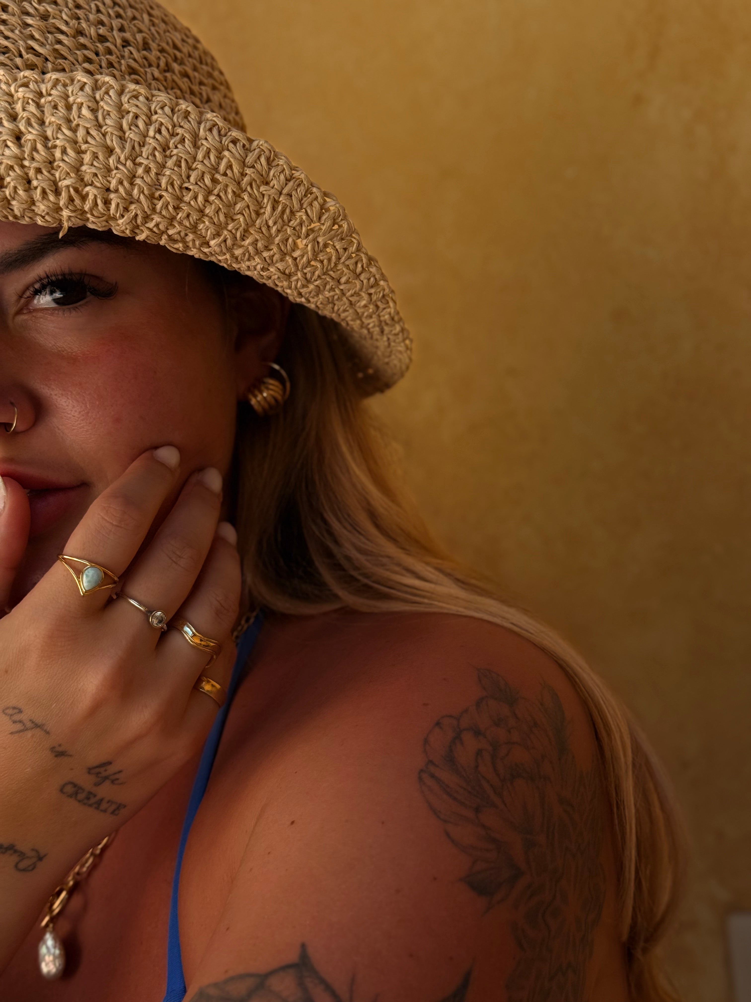 Woman wearing a straw hat and gold jewelry against a beige background