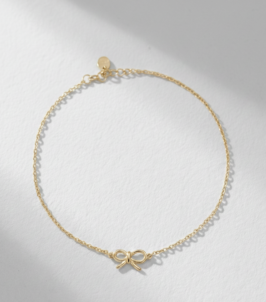 Gold necklace with a bow charm on a light gray background