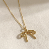 Gold bow-shaped pendant necklace on a light background