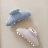 Two hair clips, one white and one blue, on a beige background.