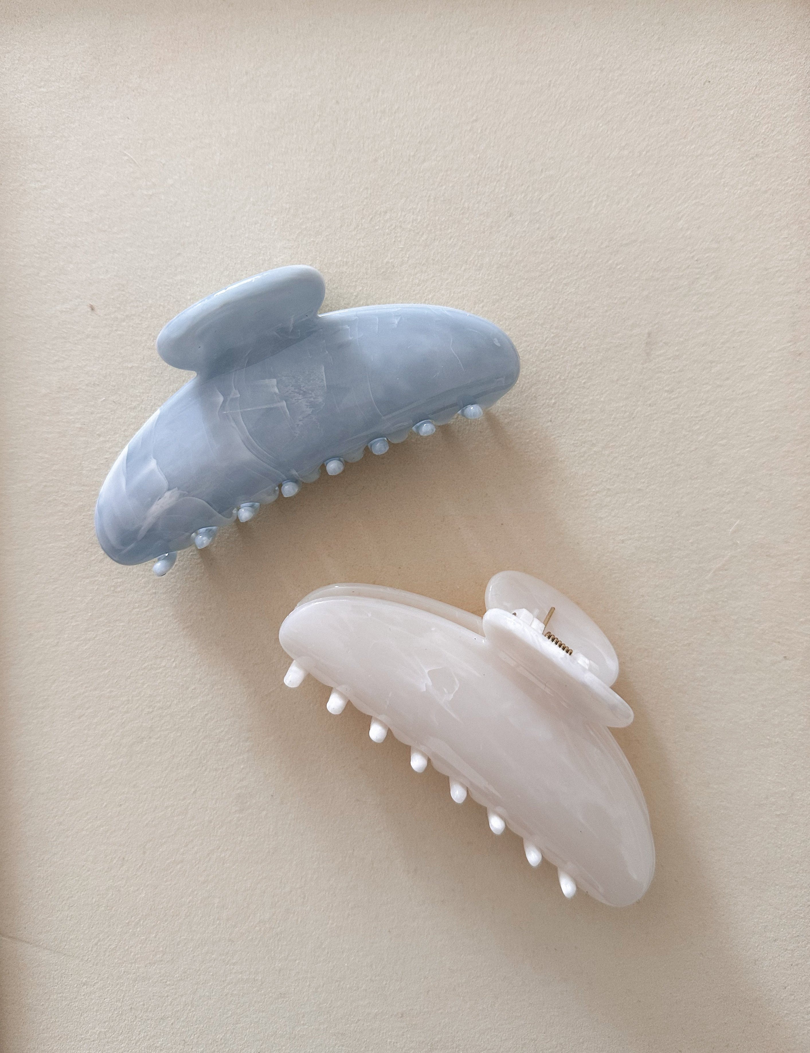 Two hair clips, one white and one blue, on a beige background.