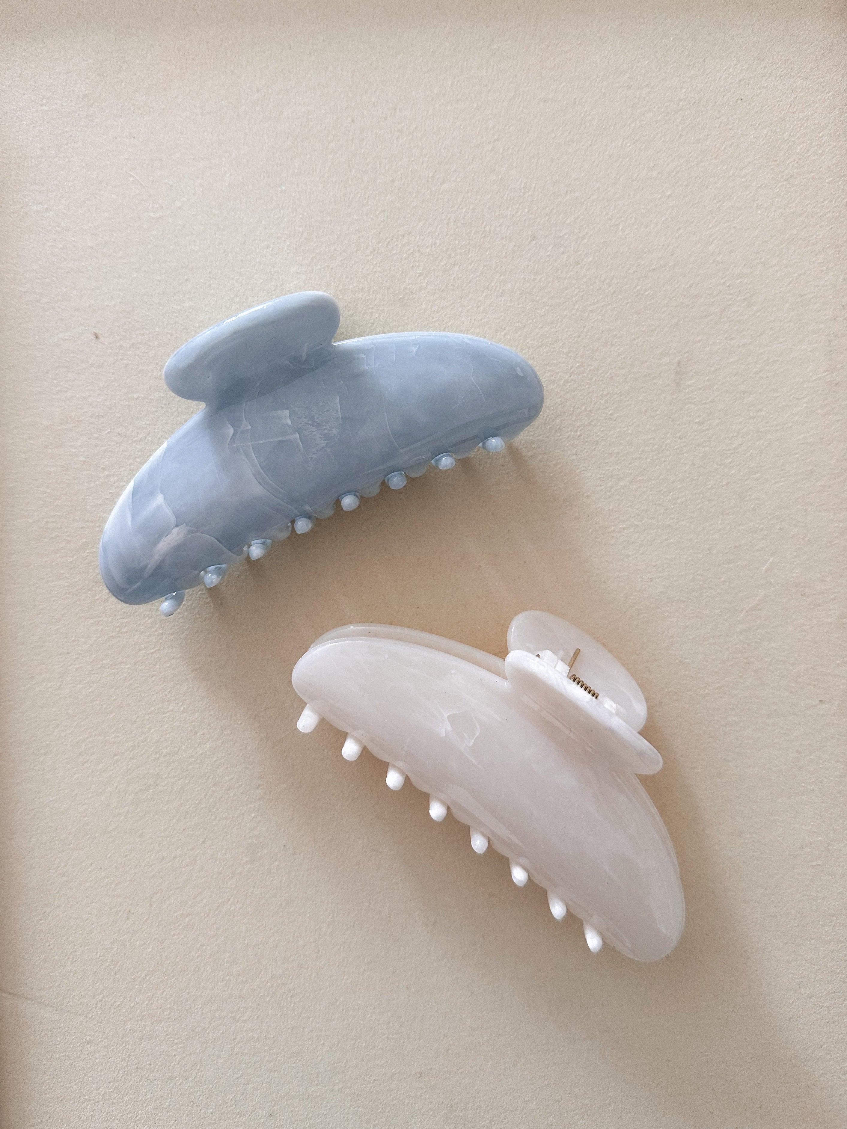 Two hair clips, one white and one blue, on a beige background.
