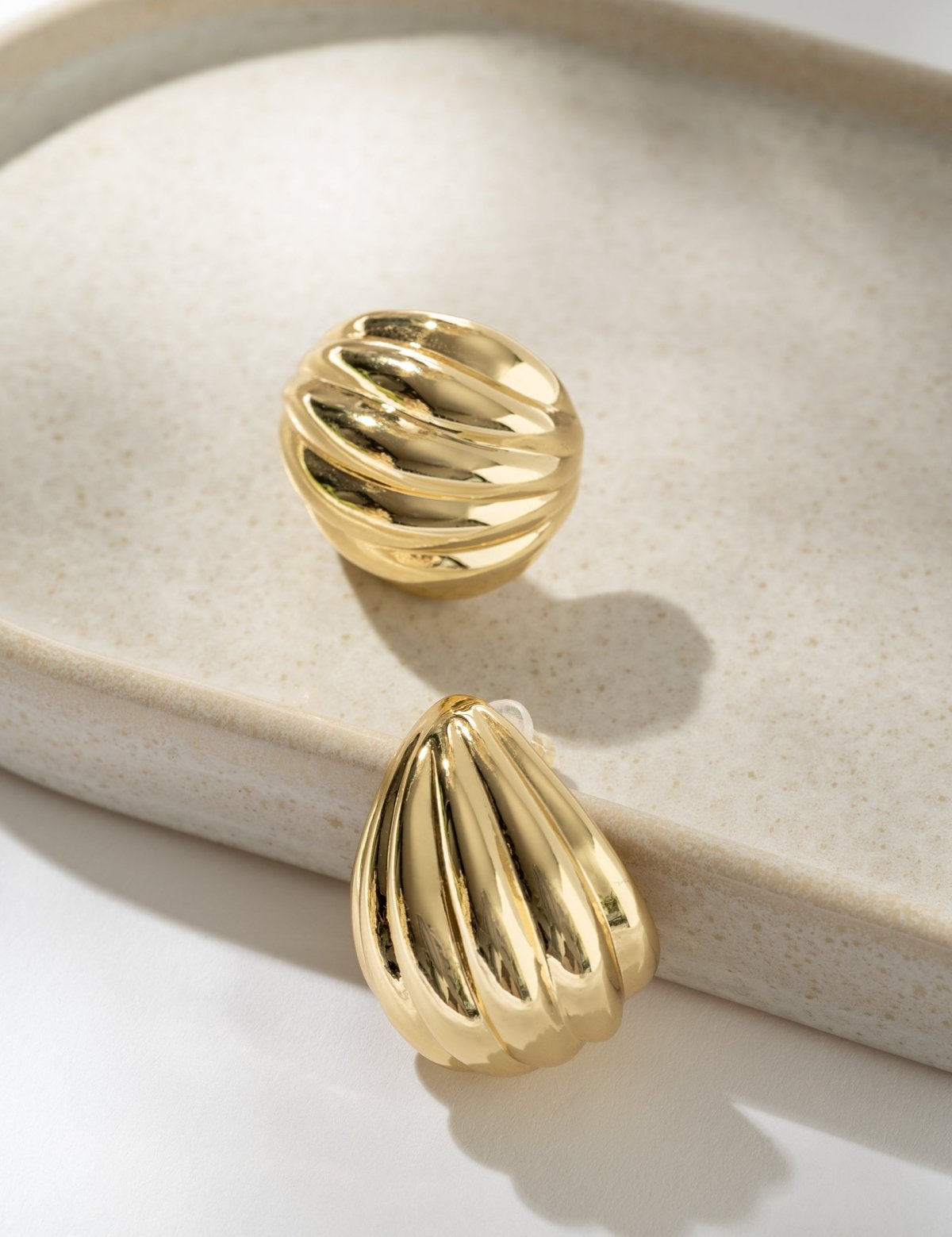 Gold earrings on a beige jewelry dish