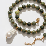 Green beaded necklace with a gold chain and white pendant on a light background