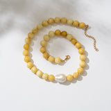 Yellow beaded necklace with a pearl pendant on a white background