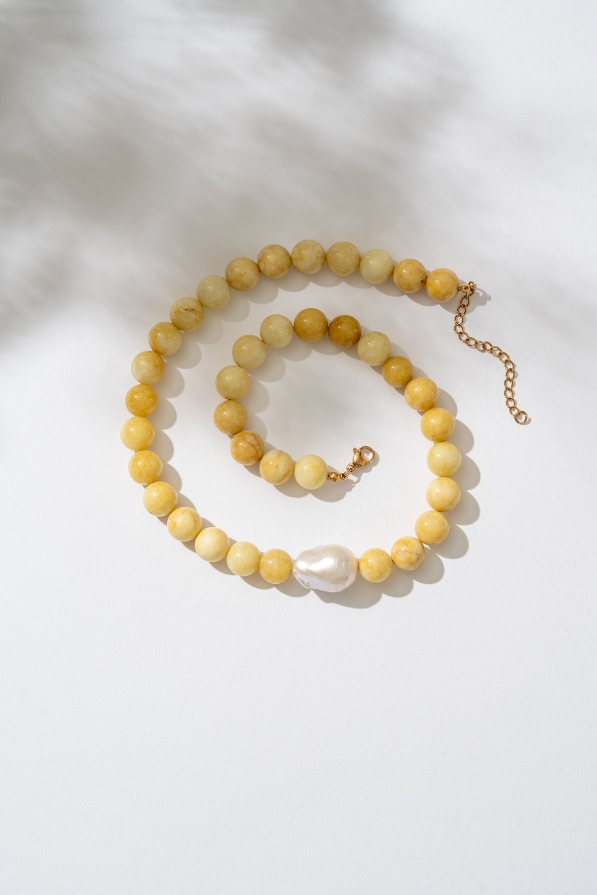 Yellow beaded necklace with a pearl pendant on a white background