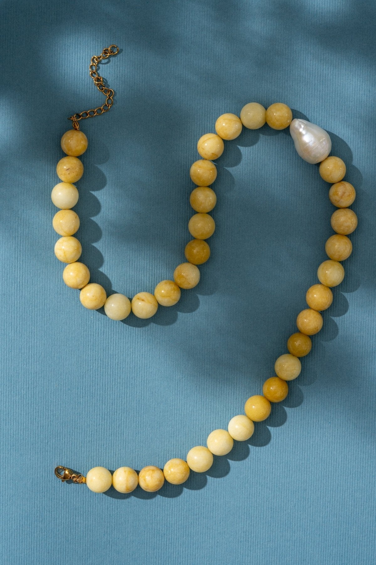 Beaded yellow necklace with a pearl on a blue background