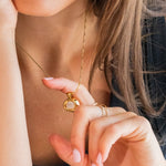 Close-up of a woman wearing a gold necklace and ring, with a blurred background.