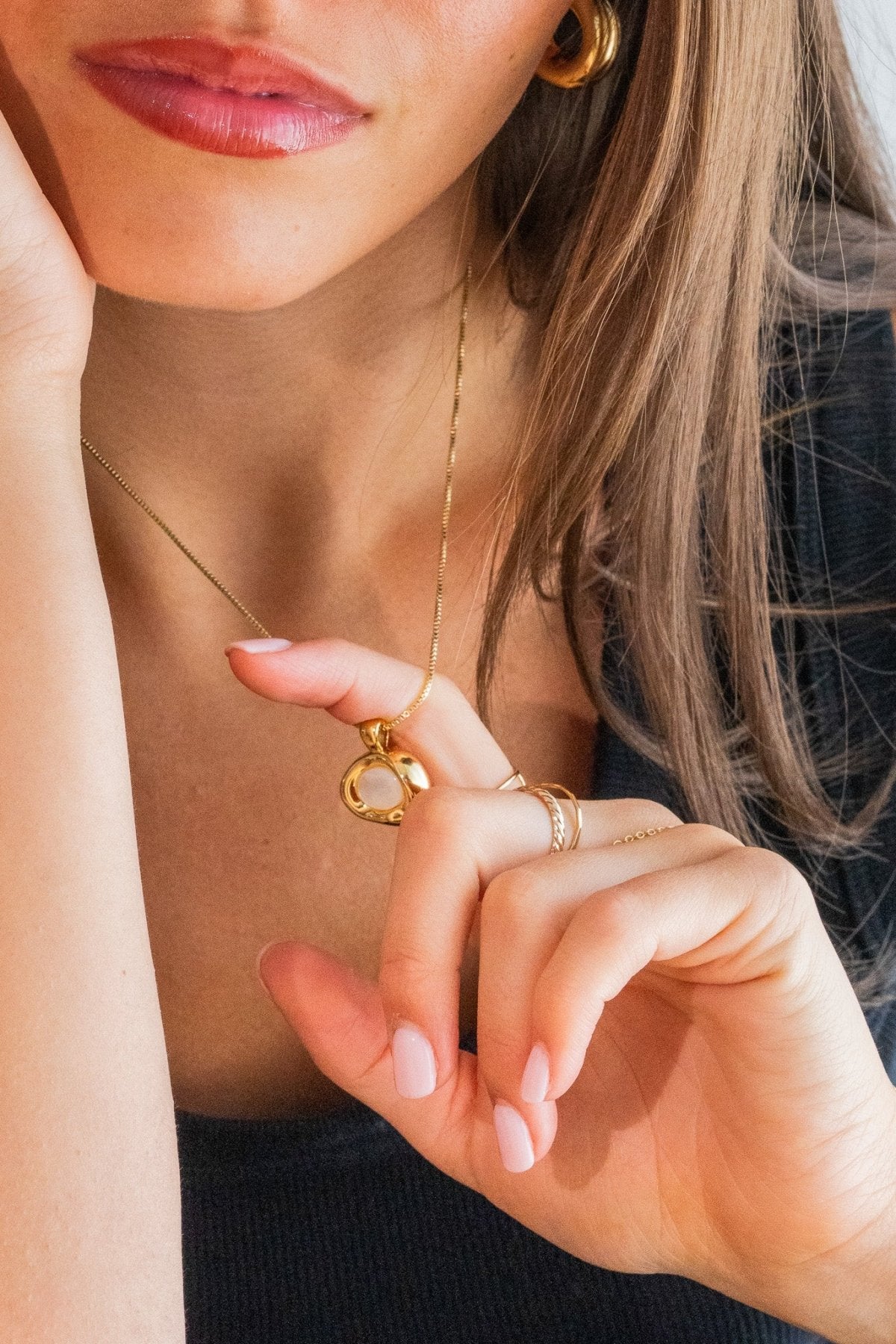 Close-up of a woman wearing a gold necklace and ring, with a blurred background.