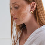 Woman with freckles wearing a white shirt and gold earrings against a light background